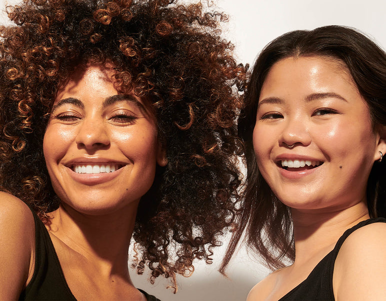 Footer of two models smiling at the camera with sunkissed, dewy skin