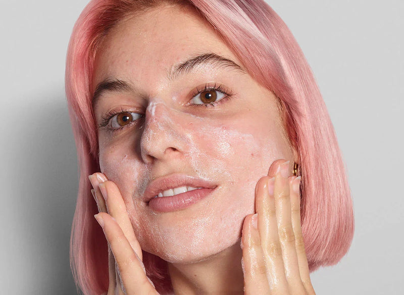 woman with pink hair washing her face
