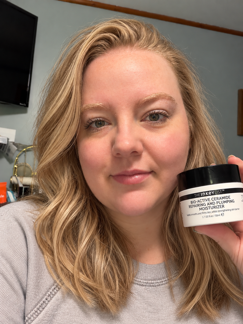 A woman with blonde hair holds up a jar of Bio-Active Ceramide Repairing and Plumping Moisturizer in front of her face.
