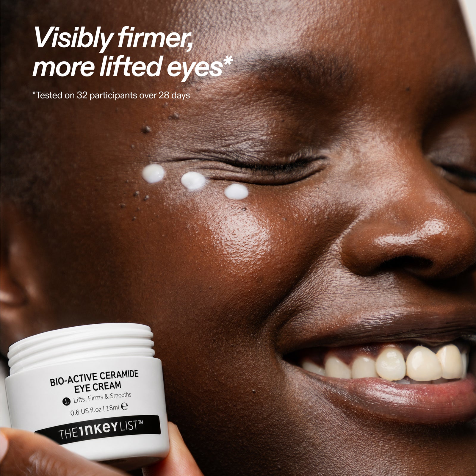 Close-up of a smiling person holding a white jar of THE INKEY LIST Bio-Active Ceramide Eye Cream, with white cream dots on their cheek and promotional text at the top.