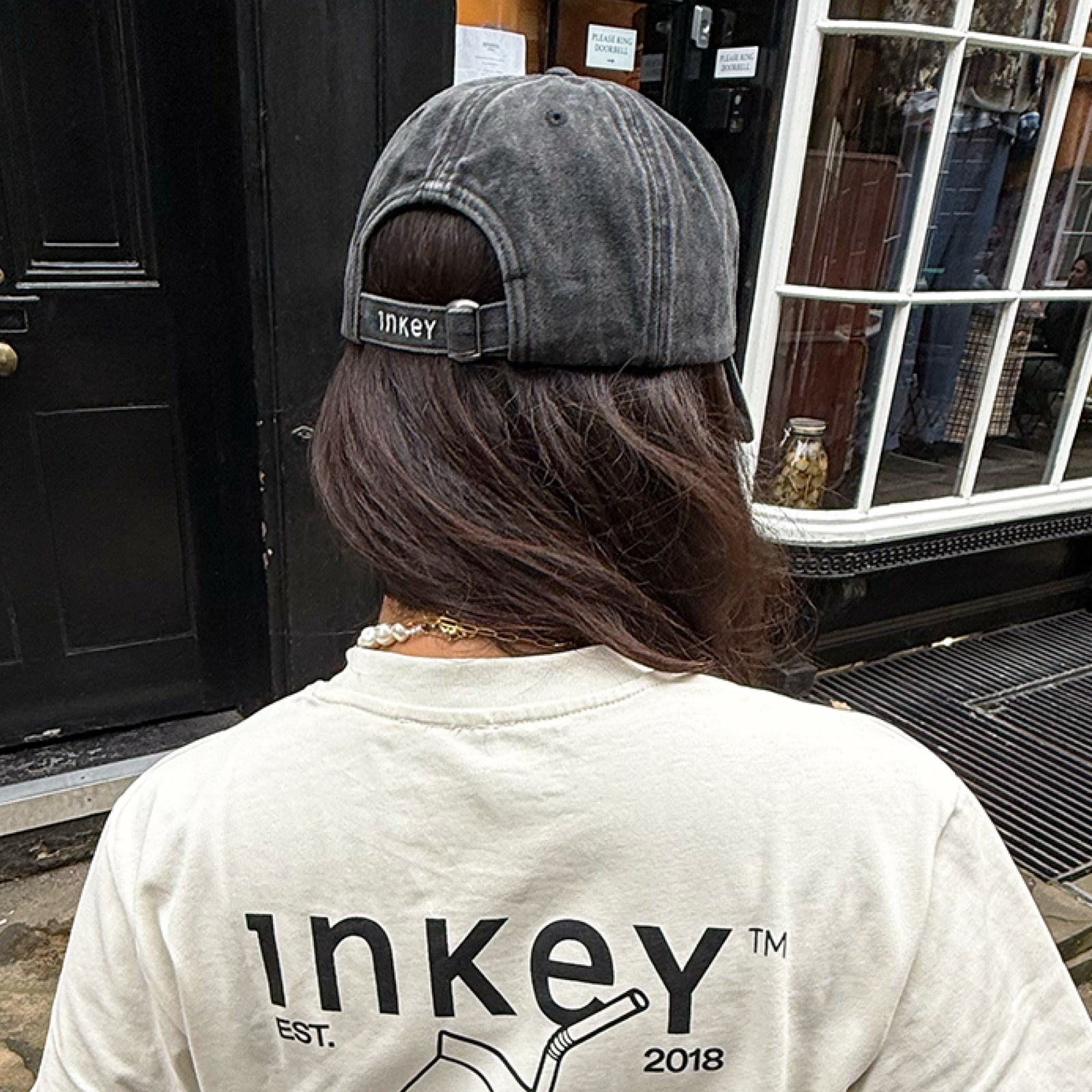 Person wearing a black cap and white shirt with 'inkey' branding in front of a store entrance.