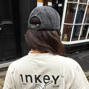 Person wearing a black cap and white shirt with 'inkey' branding in front of a store entrance.