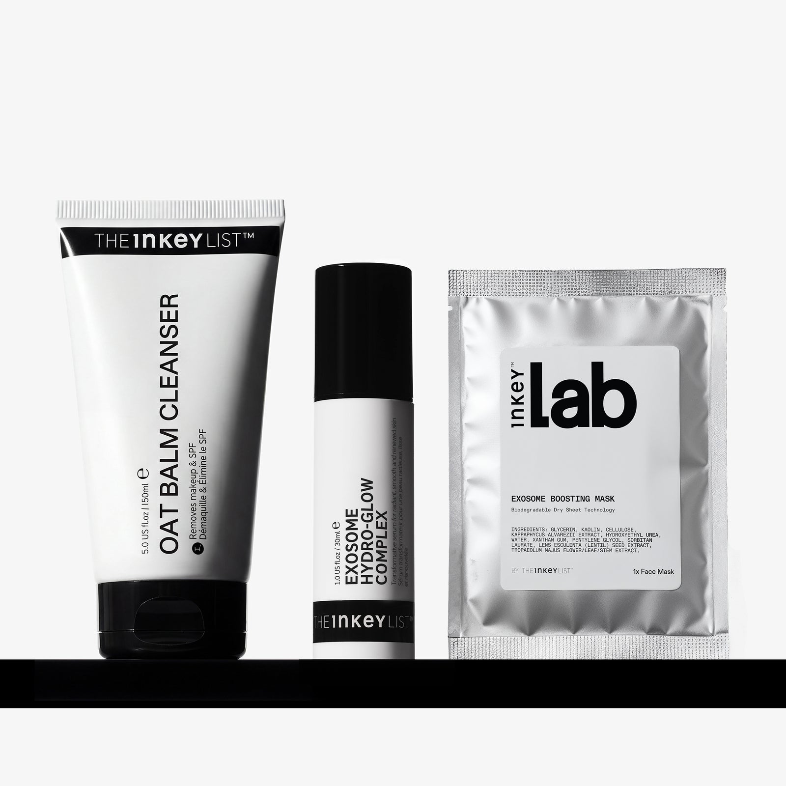 Three skincare products from The Inkey List arranged on a black shelf against a light gray background: a oat Balm Cleanser tube, an Exosome Complex bottle, and an Exosome Boosting Mask sachet.