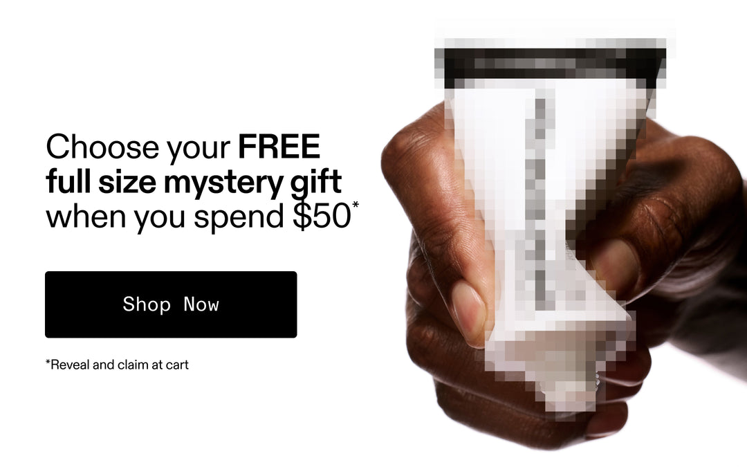 Hand holding a small container with promotional text for a free full-size mystery gift when spending $50.