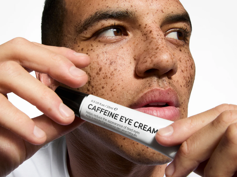 Person holding a bottle of caffeine eye cream close to their face
