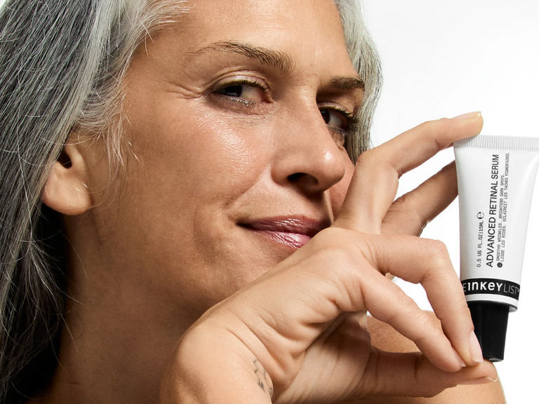 Woman holding a tube of Inkey List skincare product against a neutral background