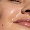 Close-up of a person's face with a glossy, hydrated complexion, showing the cheek, nose, and lips with a shiny, dewy finish.
