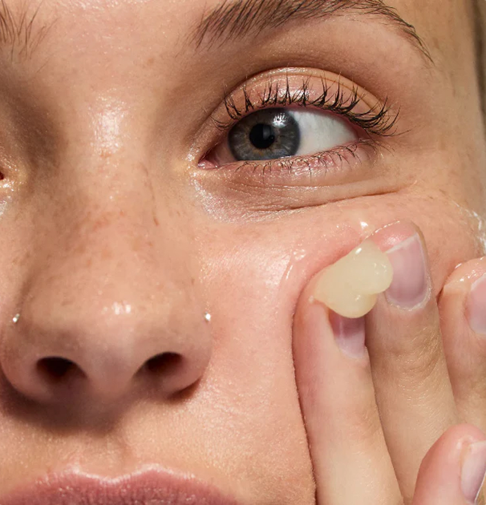 Close-up of a person applying a translucent beige gel or patch to their cheek with their fingers.